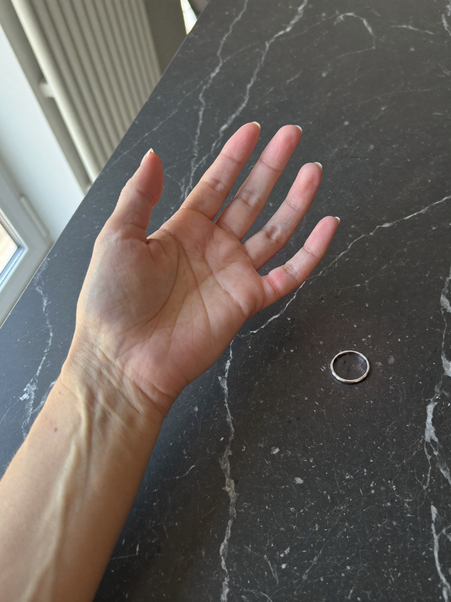 A hand resting on a dark marble worktop beside a slim silver ring