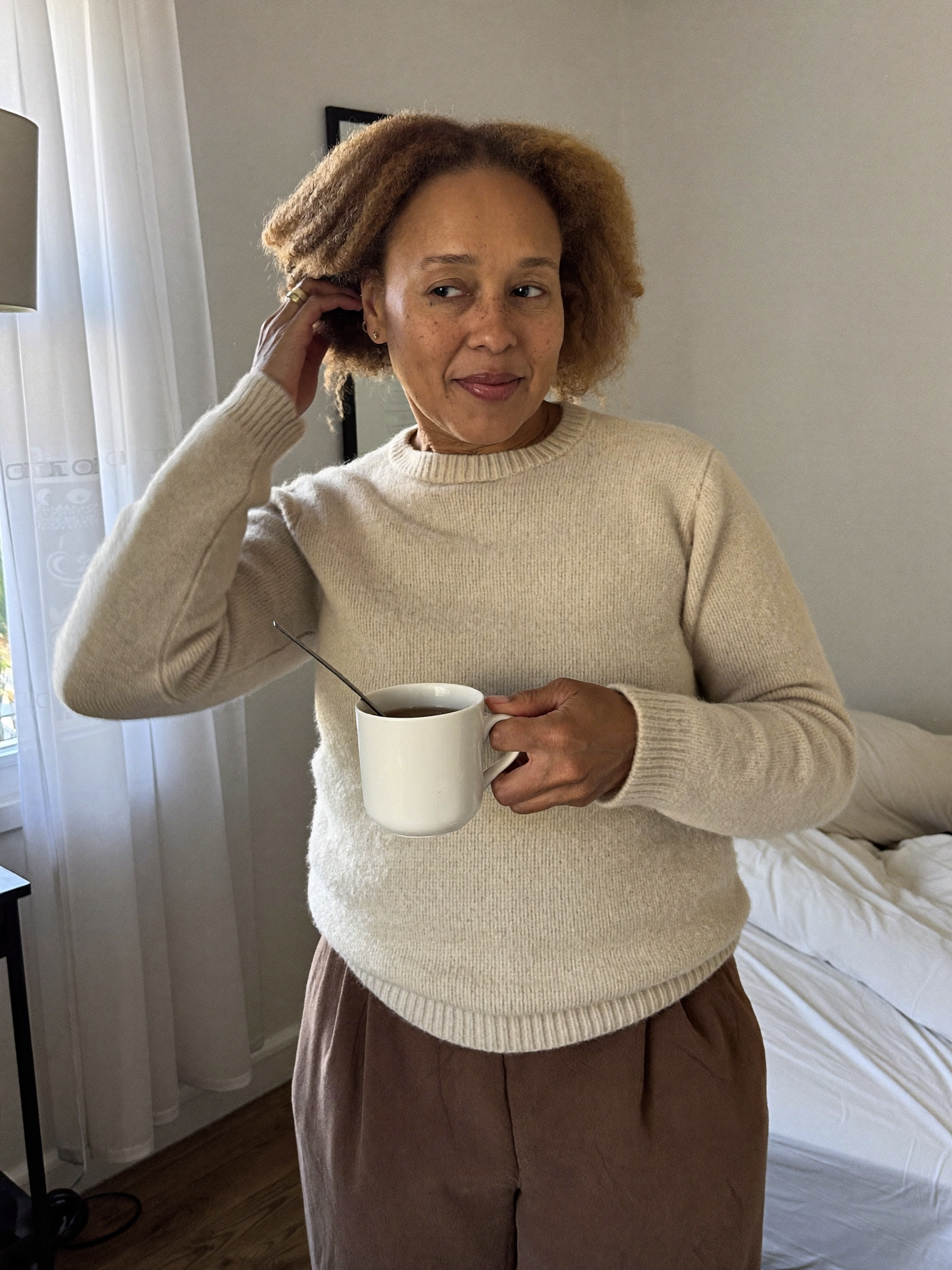 A woman in a cream jumper holding a mug of tea in soft morning light